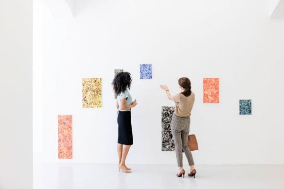 Two women in front of a wall with several paintings in a gallery