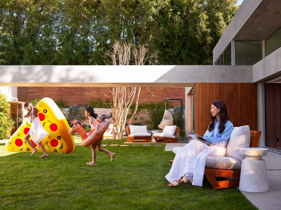 A mother is watching her 2 daughters by the pool, and one is carrying a floating pizza
