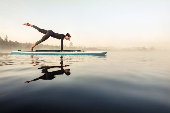 A woman in a wetsuit balances on a surfboard on a lake