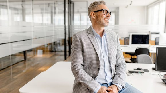 Man with glasses sitting on a drafting table in office