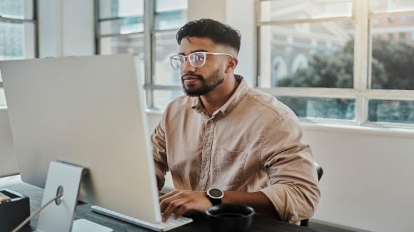 Thirty-something man seated at desk, working on computer.