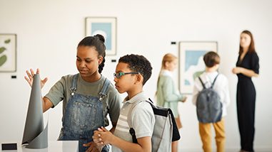 Group of diverse school-age children at an art museum interacting with an art display.