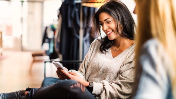 Two women engaged in a conversation about investing, with one of them checking her portfolio on her phone.