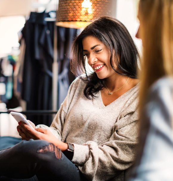 Two women engaged in a conversation about investing, with one of them checking her portfolio on her phone.