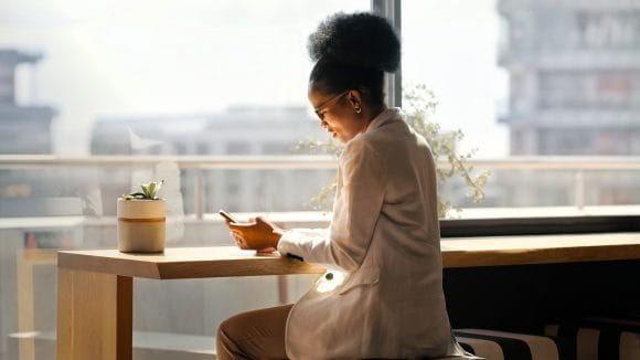 African American woman looking at her smartphone in front of a large window