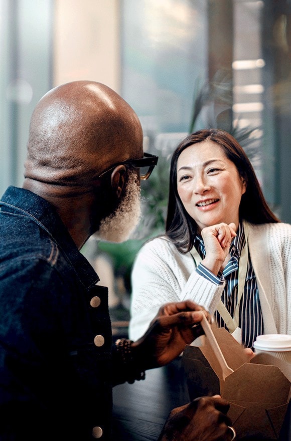Man in foreground speaking with woman indoors.
