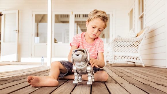 Young boy on front porch of house playing with robot dog