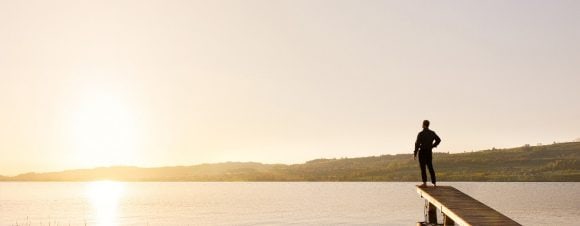 Man on lake front dock, looking out into sunset