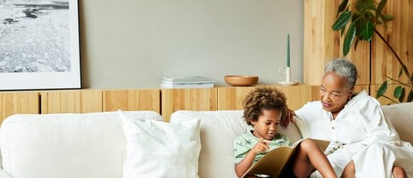 African American child reading a book with his grandmother on the couch
