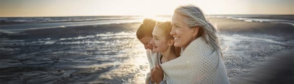 Grandmother, mother and daughter wrapped in a blanket on the beach