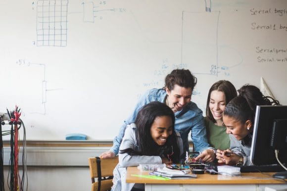 Female teacher and high school teenage students preparing robot on desk in classroom