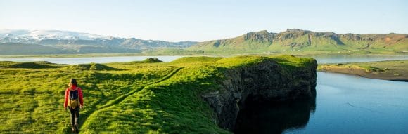 Man walking on a green small path on top of a hill with panorama view on a big lake.