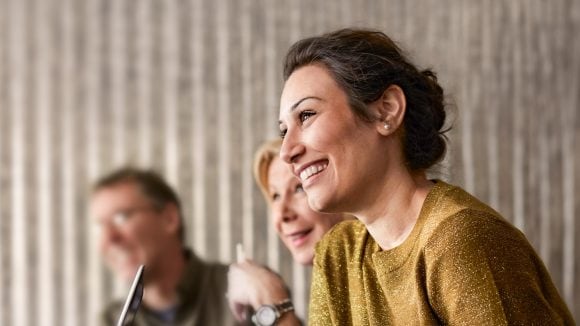 Smiling woman engaged in conversation with two others in professional setting.