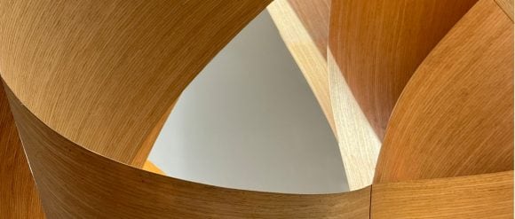 Large wooden forms of a warm golden hue interlocking around a central open space of light blue.